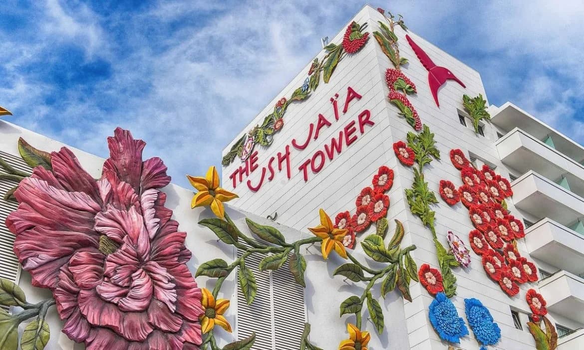 Building known as The Ushuaïa Tower adorned with large, colorful flower sculptures on its exterior walls against a blue sky backdrop.