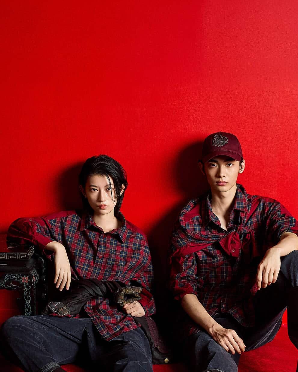 Two people wearing matching red plaid shirts sit against a vibrant red background.