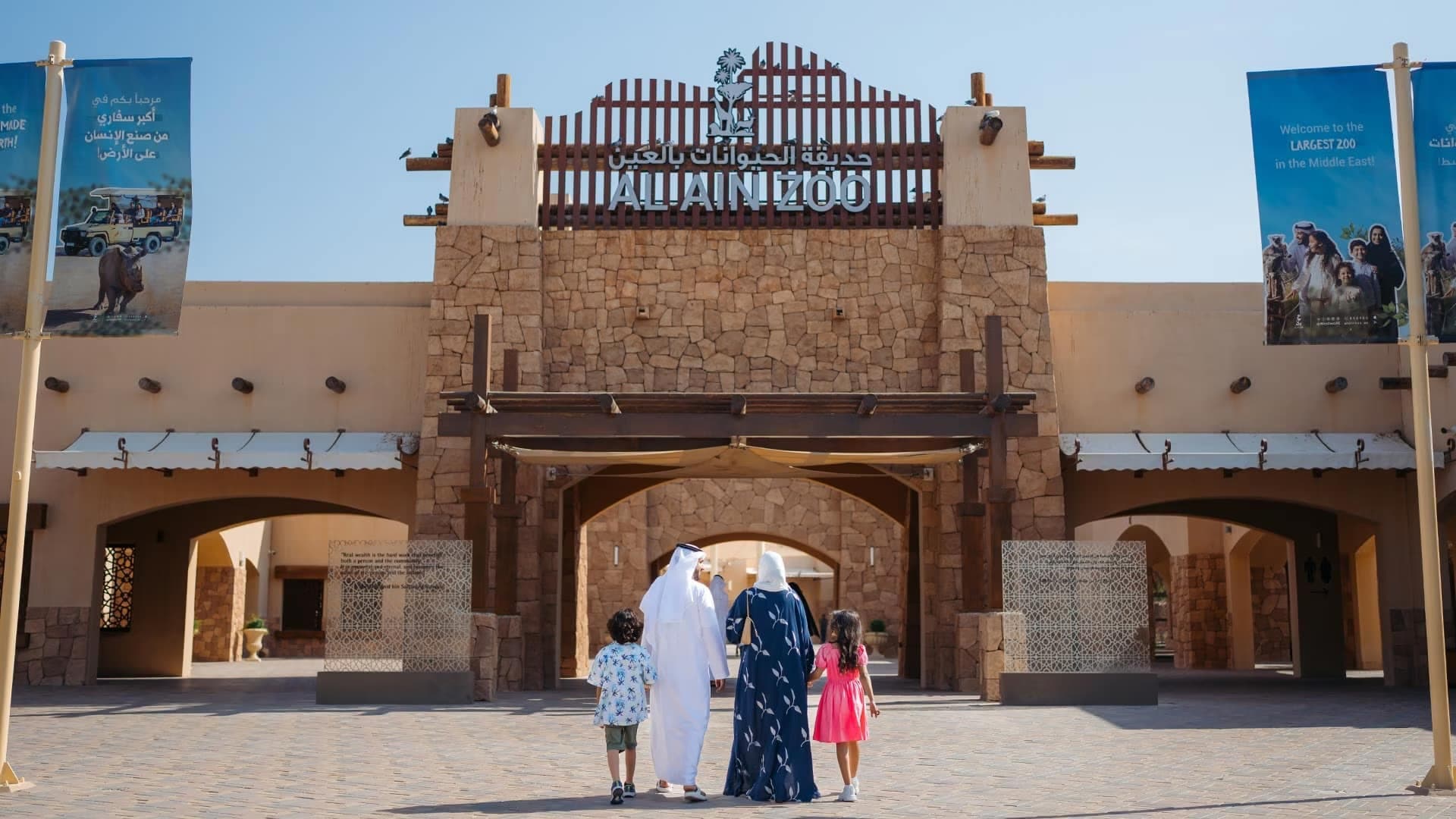 Family walking toward the entrance of Al Ain Zoo under a clear blue sky