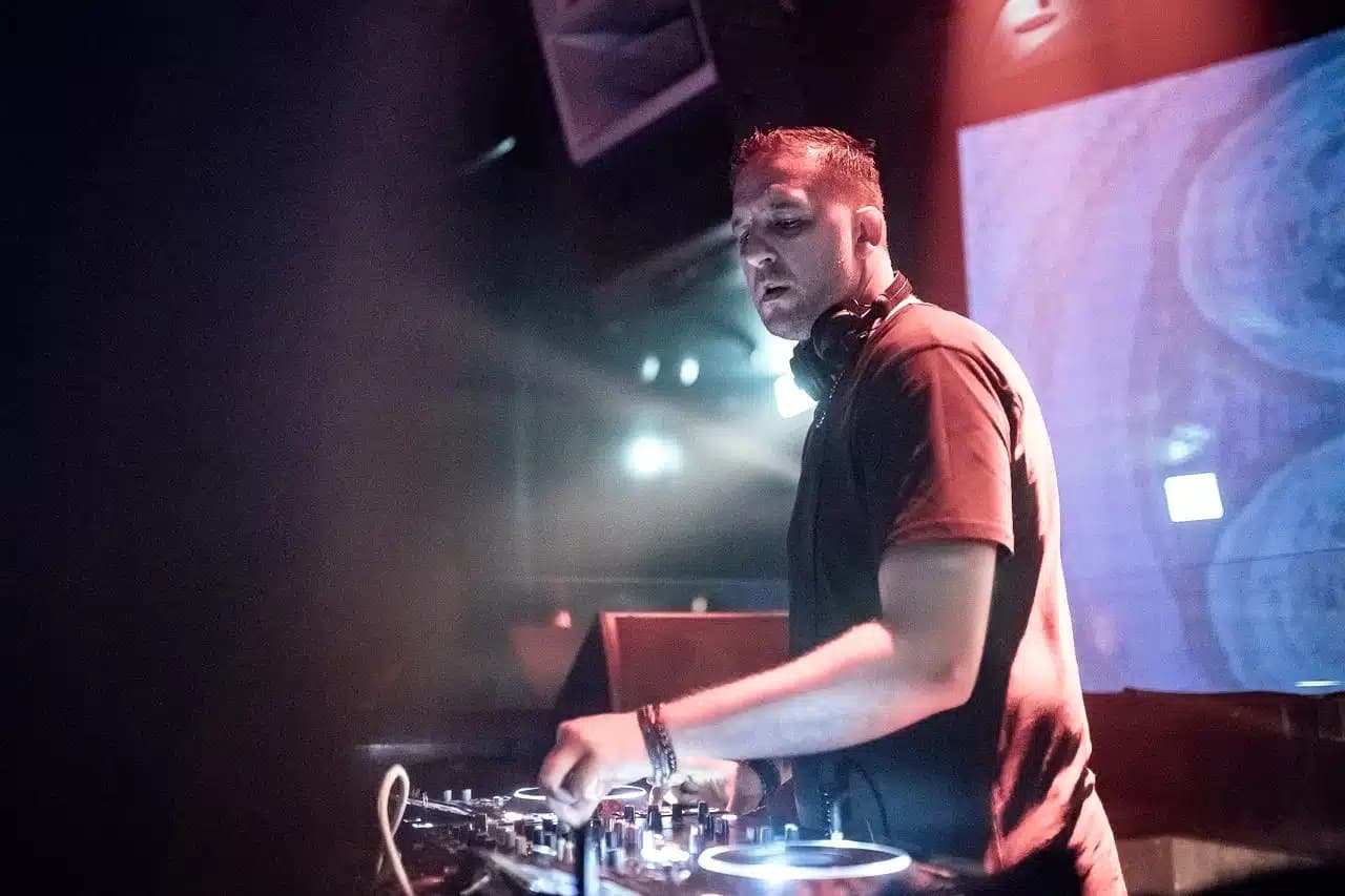 DJ mixing music at a club console under colorful stage lights