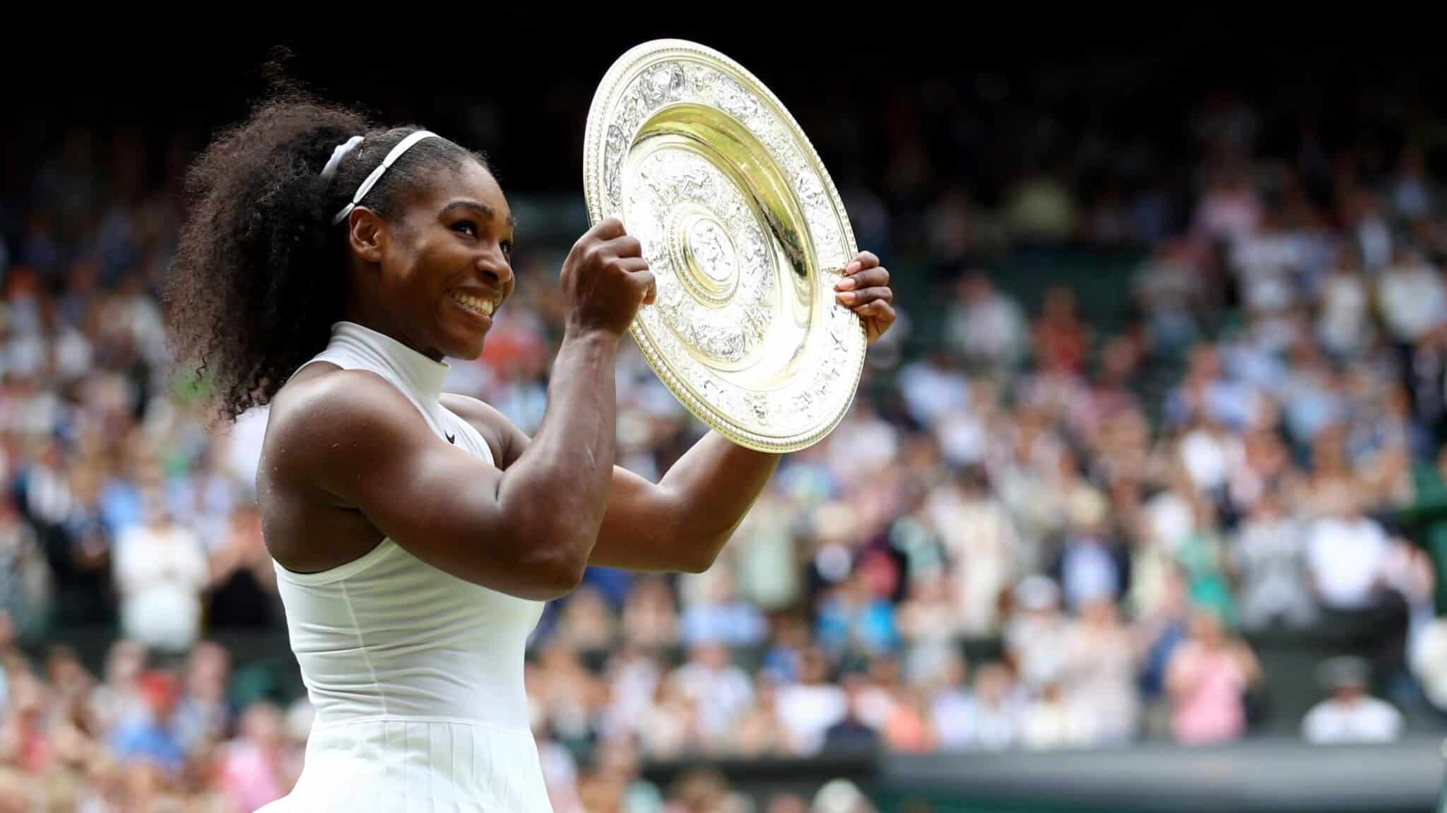 Tennis player Serena Williams smiling and holding up the Wimbledon championship trophy after a win