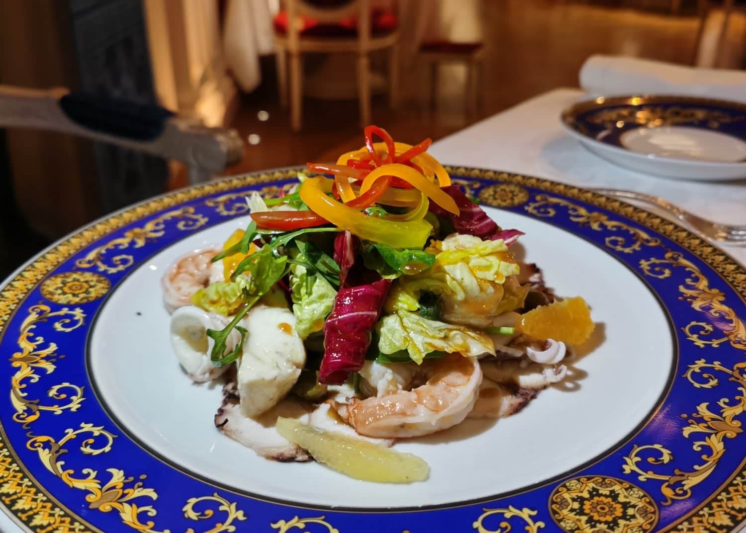 Gourmet seafood salad topped with colorful bell pepper ribbons on a blue-and-gold ornate plate