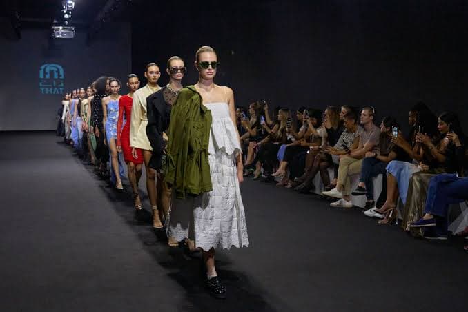 Models walk a runway in a fashion show as an audience watches from both sides