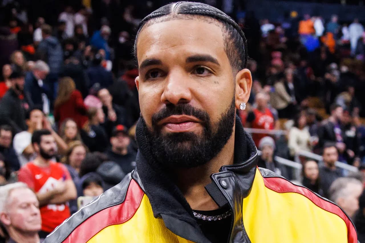 A person with braids and a beard wearing a yellow and red jacket, surrounded by a crowd in an indoor setting.