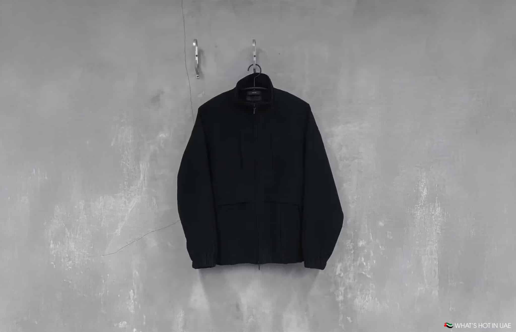 A black jacket hanging on a hanger against a textured gray wall.