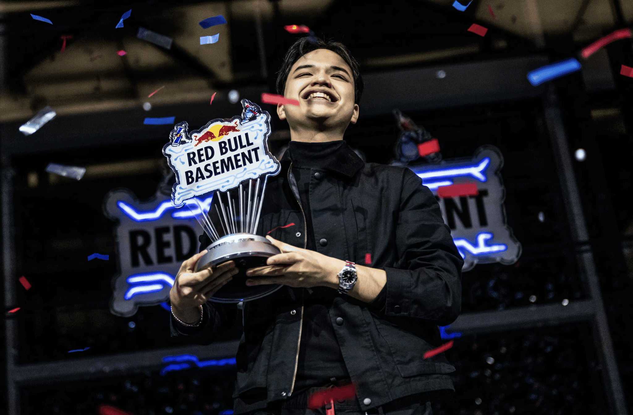 A person holding a Red Bull Basement trophy, smiling, with confetti falling around them.